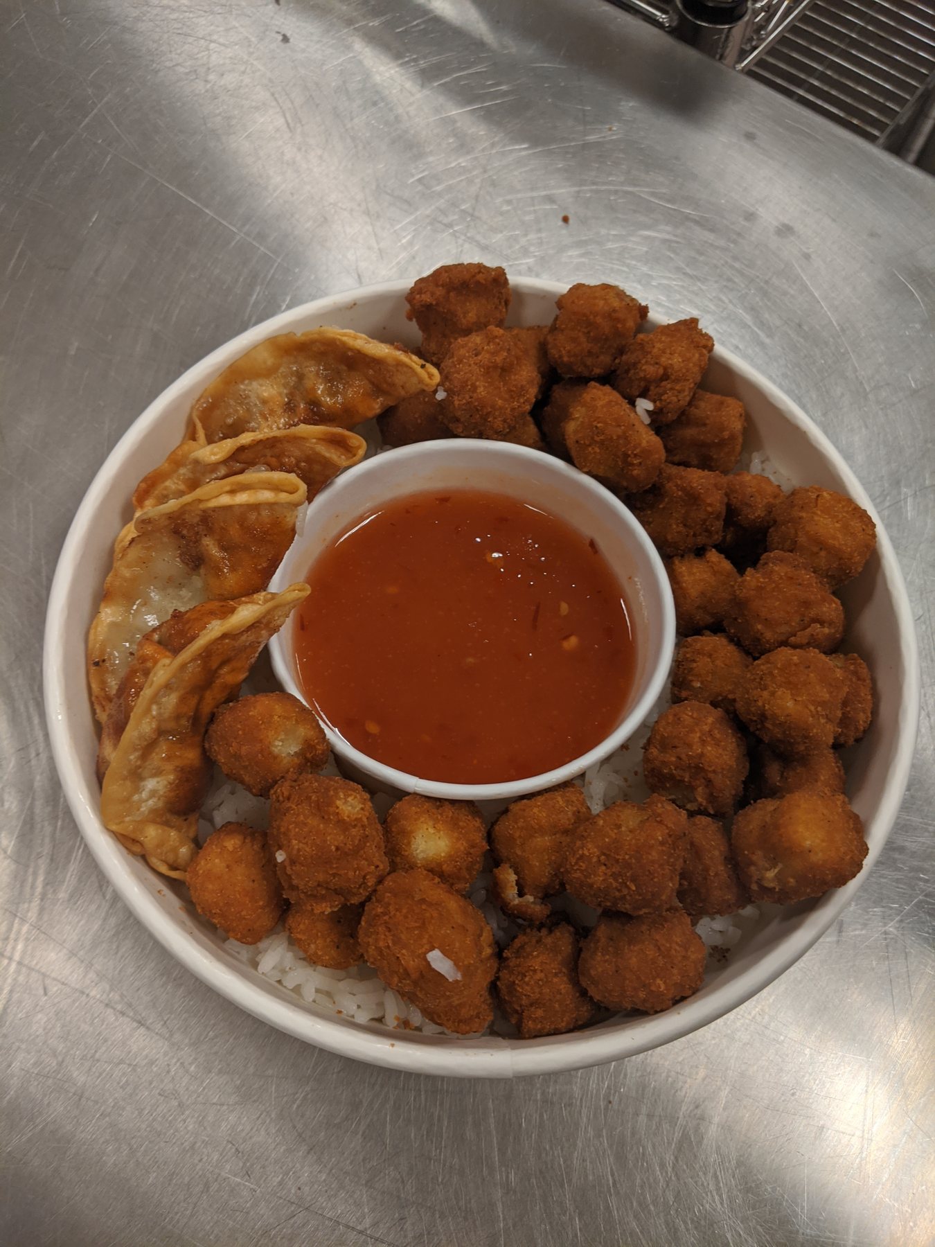 A bowl of fried chicken and wontons over rice with a dish of red sauce