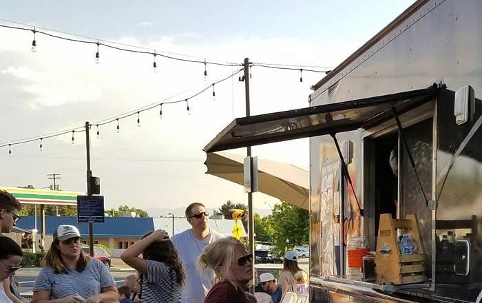 A crowd waiting at a food truck's service window under string lights at dusk