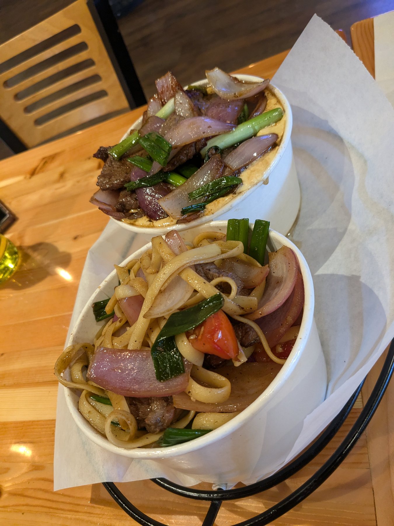 Bowls of noodles with beef, onion and spring greens on a wooden table